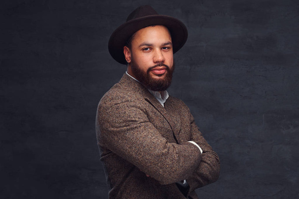 エレガントな茶色のジャケットと帽子でハンサムなアフリカ系アメリカ人男性のスタジオ ポートレート. - 写真・画像