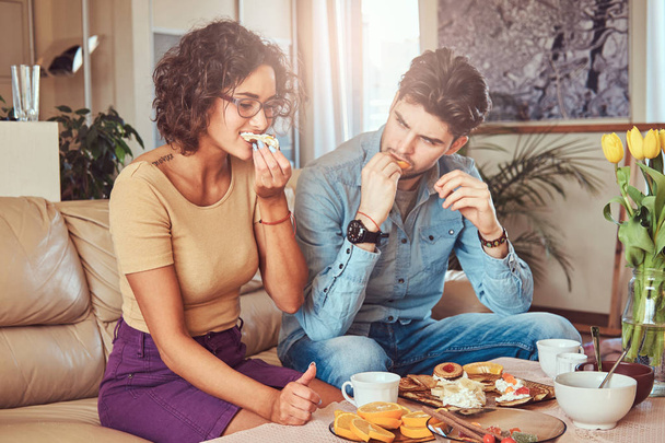 Attractive couple, handsome bearded stylish guy and curly beauty girl eating a meal at home. - Zdjęcie, obraz
