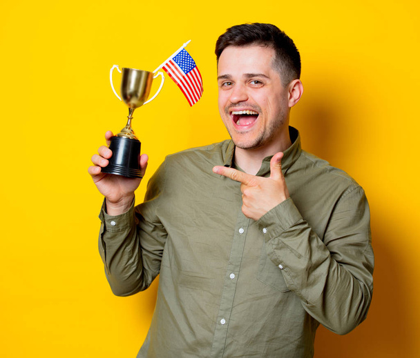 Молодой человек с американским флагом и золотой чашкой на синем фоне
 - Фото, изображение