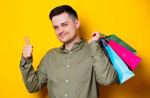 Young happy man with colorful shopping bags on yellow background - 写真・画像