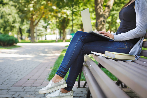 Plan recadré d'une jeune femme brune sur un banc, travaillant avec un ordinateur portable dans le parc
 - Photo, image