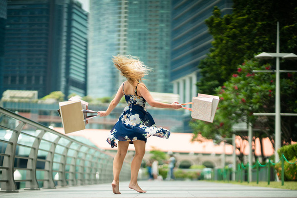 The Joy of Shopping... Excited Beautiful Woman  wearing casual blue dress with flowers, shopping bags in the streets with skyscrapers  - Foto, imagen