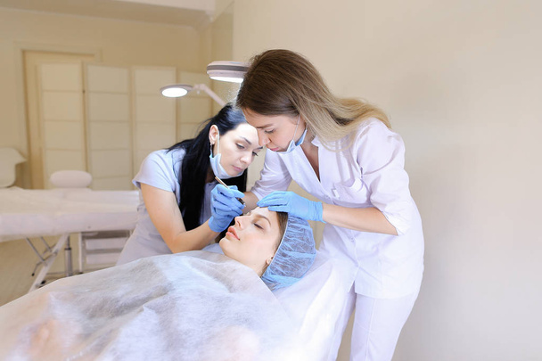 Joven mujer americana visitando a cosmetóloga y enfermera para tatuar cejas por pluma
. - Foto, imagen