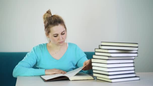 Girl student chooses a phone, pushing a stack of books on the table. - Imágenes, Vídeo