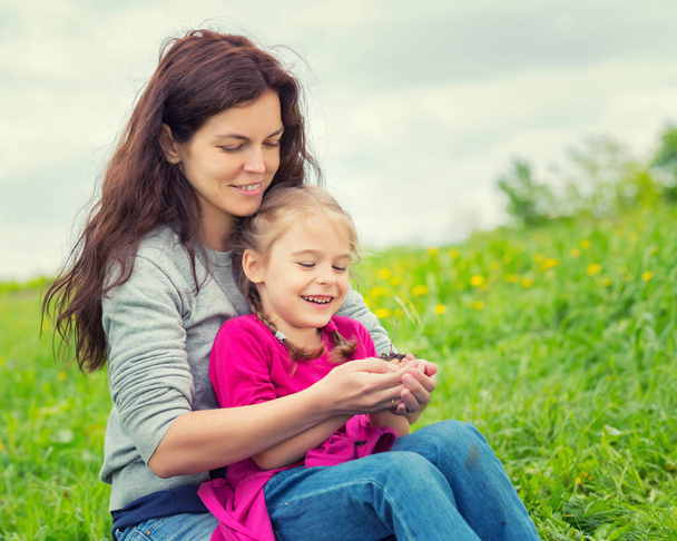Mother and daughter holding little green plant in hands - Foto, afbeelding