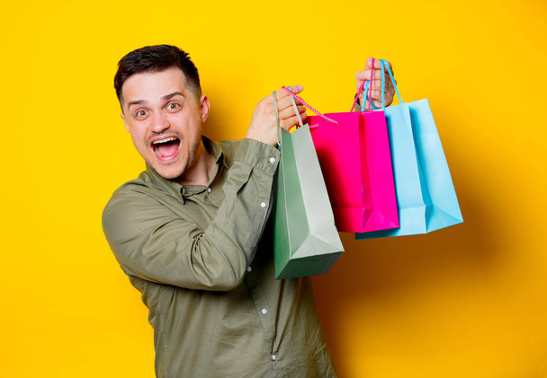 Sarı arka plan üzerinde renkli alışveriş torbaları ile mutlu delikanlı - Fotoğraf, Görsel