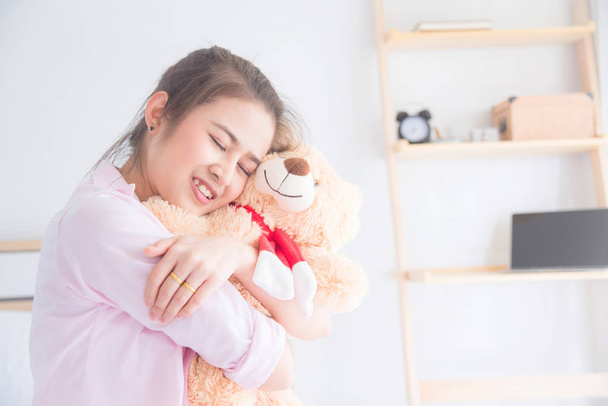 Young beautiful asian woman hugging teddy bear and smiles - Фото, изображение