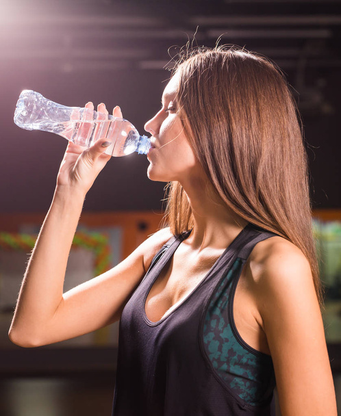 Jonge vrouw drinkwater fitness in de sportschool. Gespierde vrouw nemen pauze na het sporten - Foto, afbeelding