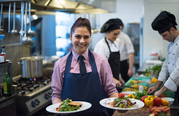 young waitress presenting dishes of tasty meals in commercial kitchen - Fotó, kép