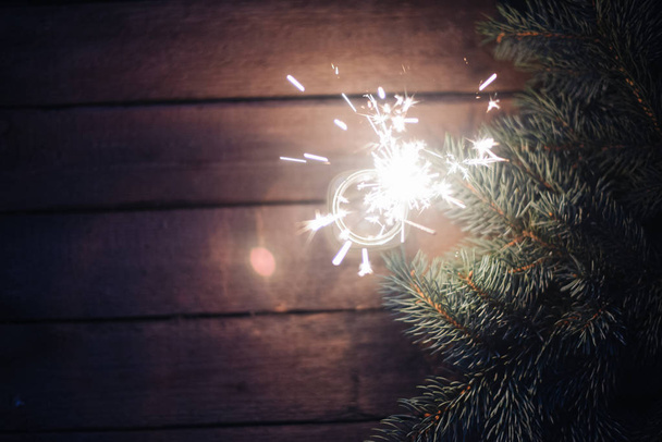 Luz de bengala em um jarro de vidro em um fundo de madeira com ramos de uma árvore de Natal
 - Foto, Imagem