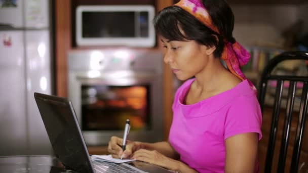 woman with laptop writing recipe from internet in kitchen - Materiał filmowy, wideo