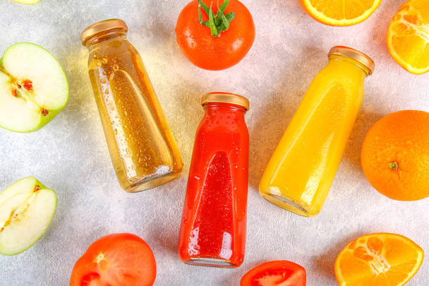 Bottles with fresh orange, apple, tomato juice on a gray concrete table. Fruits and vegetables around. Top view. Flat Lay. - Foto, immagini