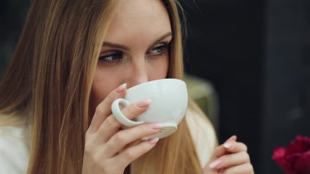 Adorable young woman drinks her coffee sitting in the cafe - Filmati, video
