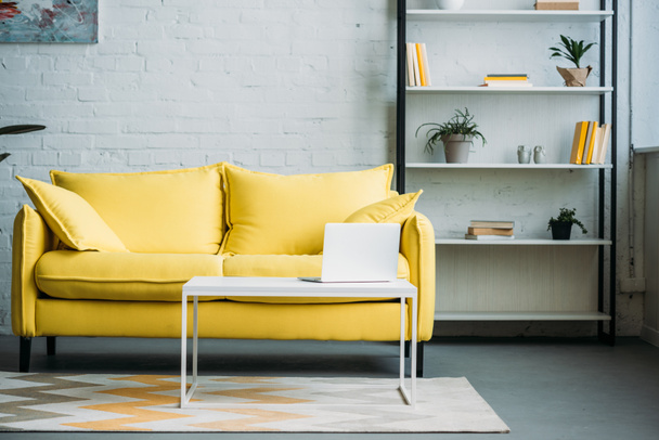 portátil en la mesa cerca de sofá amarillo en la sala de estar
 - Foto, Imagen