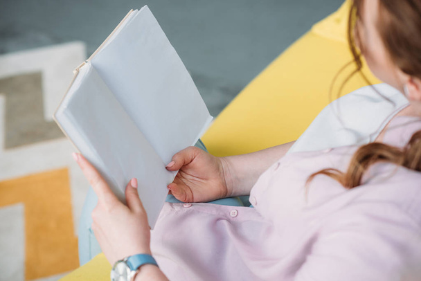 обрезанный образ женщины, читающей книгу на диване дома
 - Фото, изображение