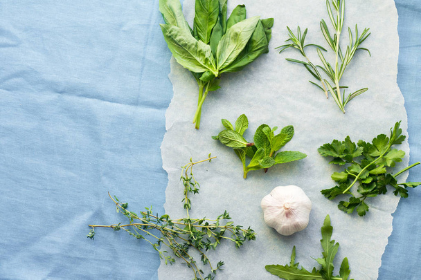 Fresh culinary herbs on blue linen background: rosemary, thyme, mint, arugula, basil and parsley in small bunches with garlic clove  - Foto, immagini