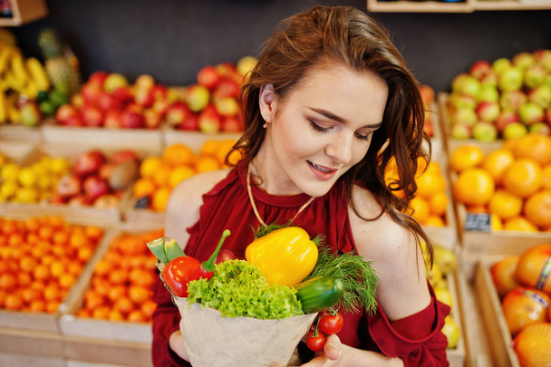 Girl in red holding different vegetables on fruits store. - Φωτογραφία, εικόνα