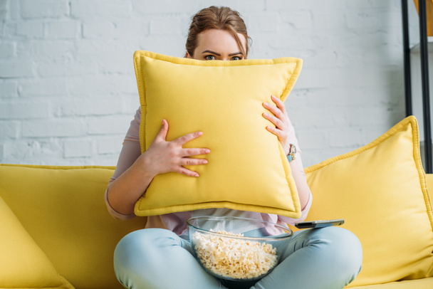 Kobieta, patrząc od poduszki, podczas oglądania filmu grozy z popcornu w domu - Zdjęcie, obraz