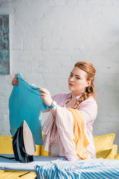 beautiful woman looking at shirt near ironing board at home - Fotó, kép