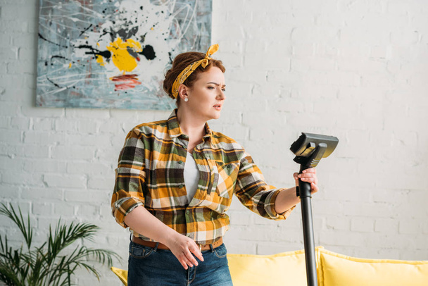 beautiful woman looking at vacuum cleaner at home - Foto, afbeelding