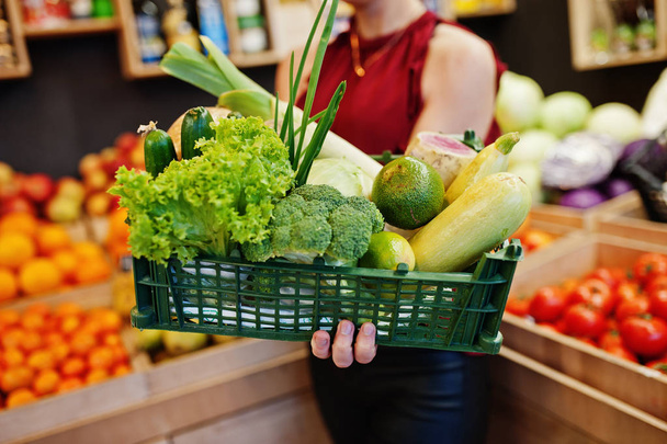 Girl in red holding different vegetables on fruits store. - Fotografie, Obrázek