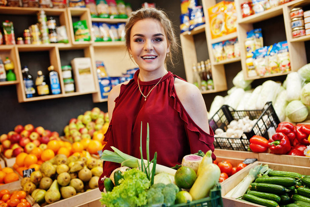 Girl in red holding different vegetables on fruits store. - Foto, Bild