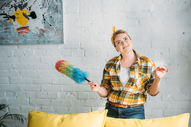pensive beautiful woman posing with colored dust brush for cleaning at home - Foto, Bild
