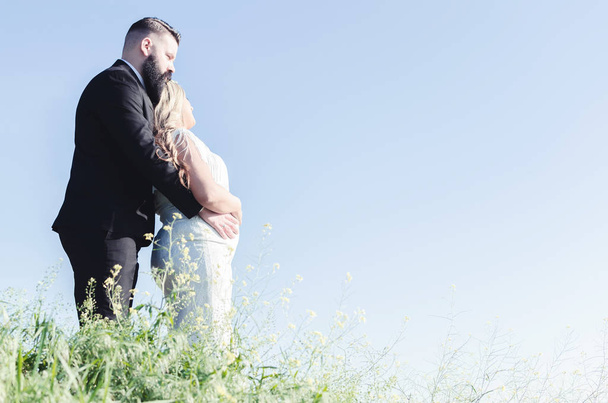 Young wedding couple standing and embracing on green meadow before blue sky - Foto, Bild