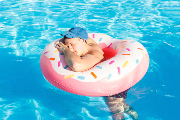 Вид сверху на молодого пьяного парня, плавающего с розовым кругом в бассейне. пьяный парень на отдыхе в отеле
 - Фото, изображение