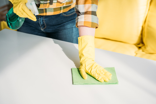 cropped image of woman cleaning table with spray bottle and rag at home - Foto, afbeelding