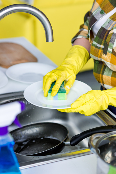 обрезанный образ женщины, моющей тарелку со стиральной губкой на кухне
 - Фото, изображение