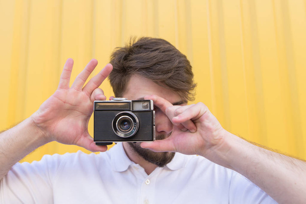 Ένας άνθρωπος φωτογραφίζει μια ρετρό κάμερα στο φόντο των έναν κίτρινο τοίχο. Πορτρέτο ενός φωτογράφου που φωτογραφήθηκαν σε μια ταινία ρετρό φωτογραφική μηχανή - Φωτογραφία, εικόνα