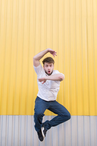Funny man jumping against the background of the yellow wall and looking at the camera. - Foto, Bild