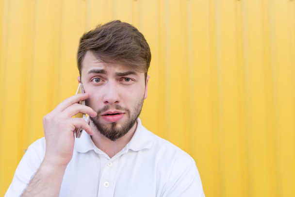 Closeup portrait of a funny man talking on the phone on a yellow background. - Photo, image