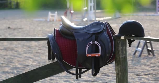 Horseback saddle on the wooden fence on the background of training riders in a sunny day - Footage, Video