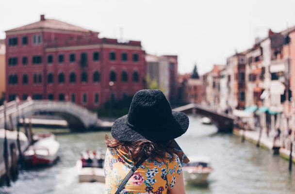 Rückansicht eines Mädchens mit Hut, das auf der Brücke über den Kanal in Venedig steht - Italien - Foto, Bild