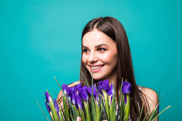 Női nap. A vidám fiatal nő, kezében iris csokor kék háttér felett elszigetelt portréja - Fotó, kép