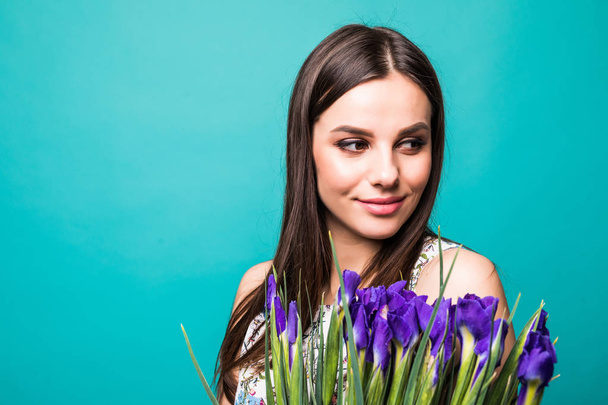 Portrait of a beautiful young woman in sweater holding bouquet of irises isolated over blue background - Photo, Image