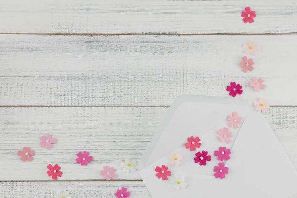 Beyaz zarf süslemeleri beyaz tahta arka plan ile kopya alanı üzerinde pembe kağıt çiçeklerle - Fotoğraf, Görsel