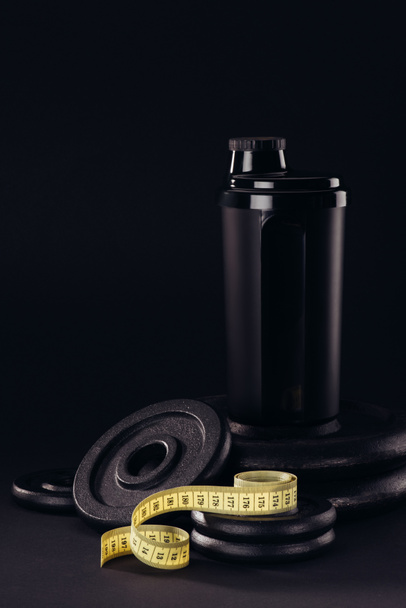 білковий шейкер з вимірювальною стрічкою та ваговими пластинами ізольовані на чорному
 - Фото, зображення