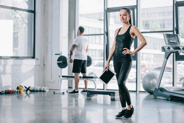 young female personal trainer with digital tablet and athletic man with barbell behind at gym - Fotoğraf, Görsel