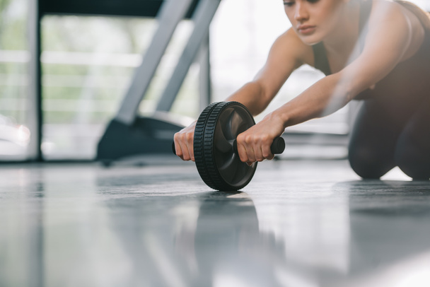cropped image of young sportswoman doing exercise with abs roller at gym - Fotoğraf, Görsel
