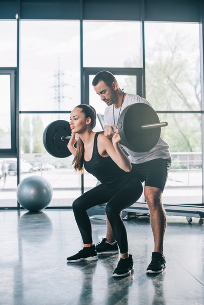 entrenador personal masculino ayudando a la deportista a hacer ejercicios con barra de pesas en el gimnasio
 - Foto, imagen