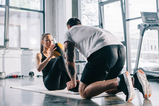 male personal trainer helping sportswoman to do abs with ball at gym - Fotoğraf, Görsel
