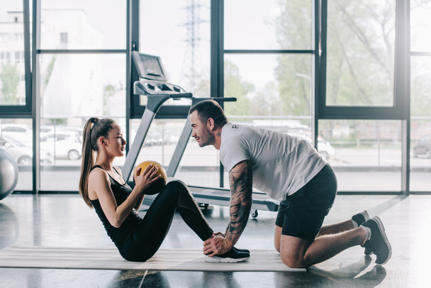 male personal trainer helping sportswoman to do abs with ball at gym - Photo, Image