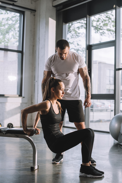 male personal trainer looking at sportswoman doing plank at gym - Φωτογραφία, εικόνα
