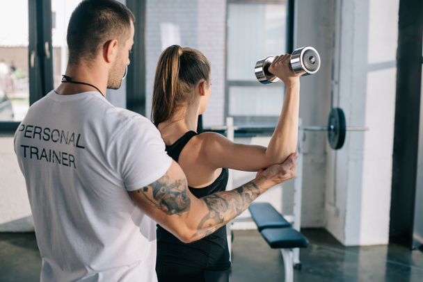 entrenador personal masculino ayudando a la deportista a hacer ejercicios con mancuerna en el gimnasio
 - Foto, imagen
