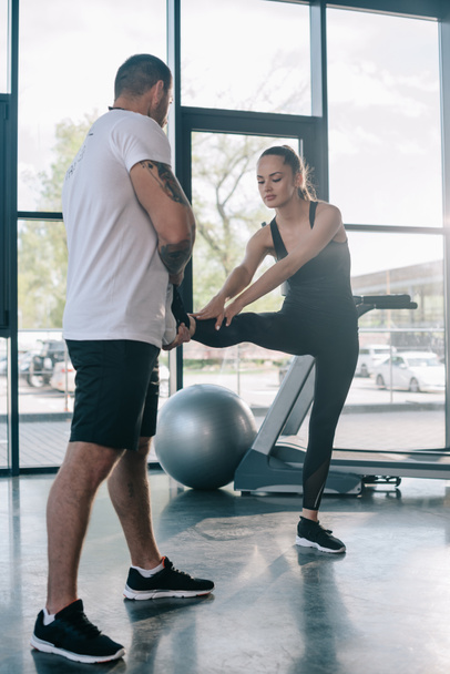 male personal trainer helping sportswoman to stretching at gym - Фото, зображення