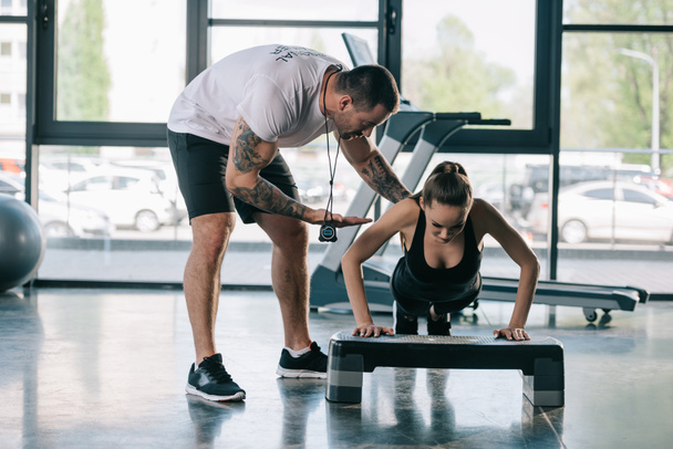 male personal trainer helping sportswoman to do push ups at gym - Foto, imagen