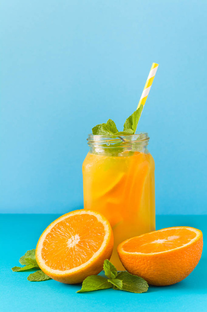 Jar with orange lemonade, decorated ice and mint on blue paper background. - Foto, Imagen